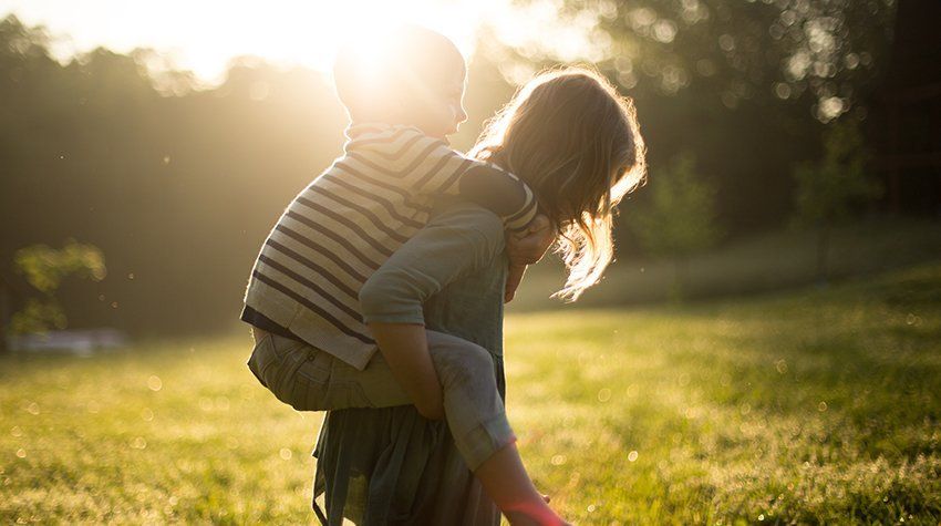 A woman is carrying a child on her back in a field.