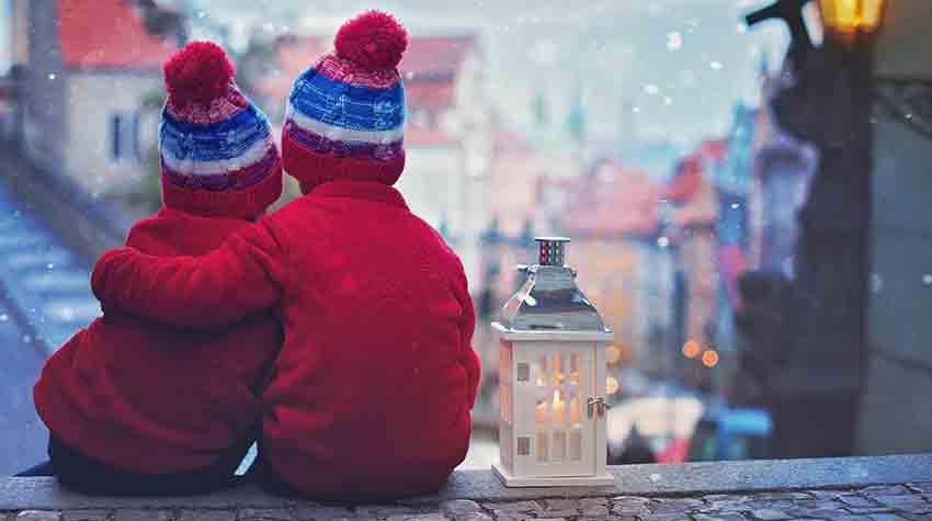 Two children are sitting next to each other on a sidewalk looking out a window at a christmas market.