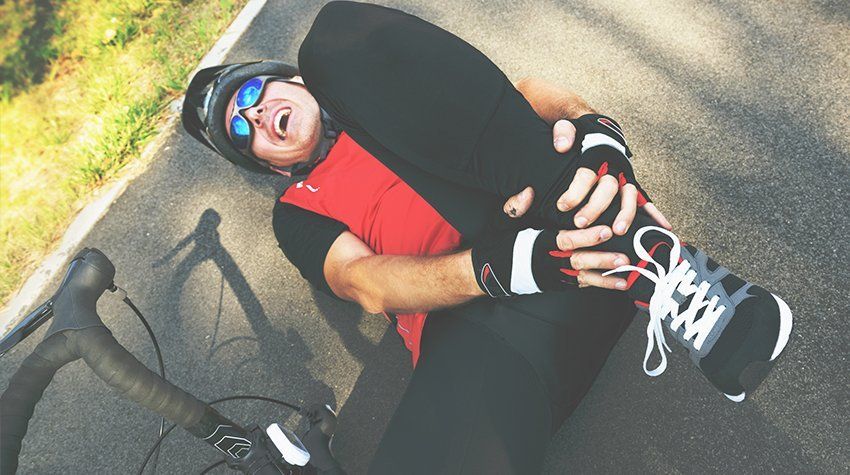 A man is laying on the ground holding his leg in pain while riding a bike.