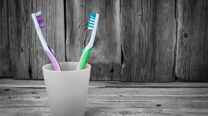 Two toothbrushes are in a glass on a wooden table.