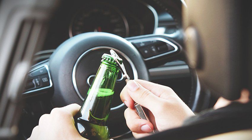 A person is holding a bottle of beer in their hand while driving a car.