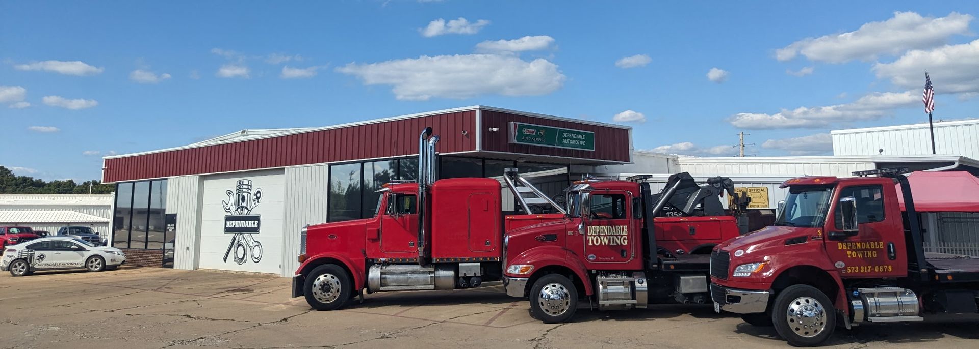 Red semi-truck parked outside a white building with red awnings in a truck lot | Dependable Automotive