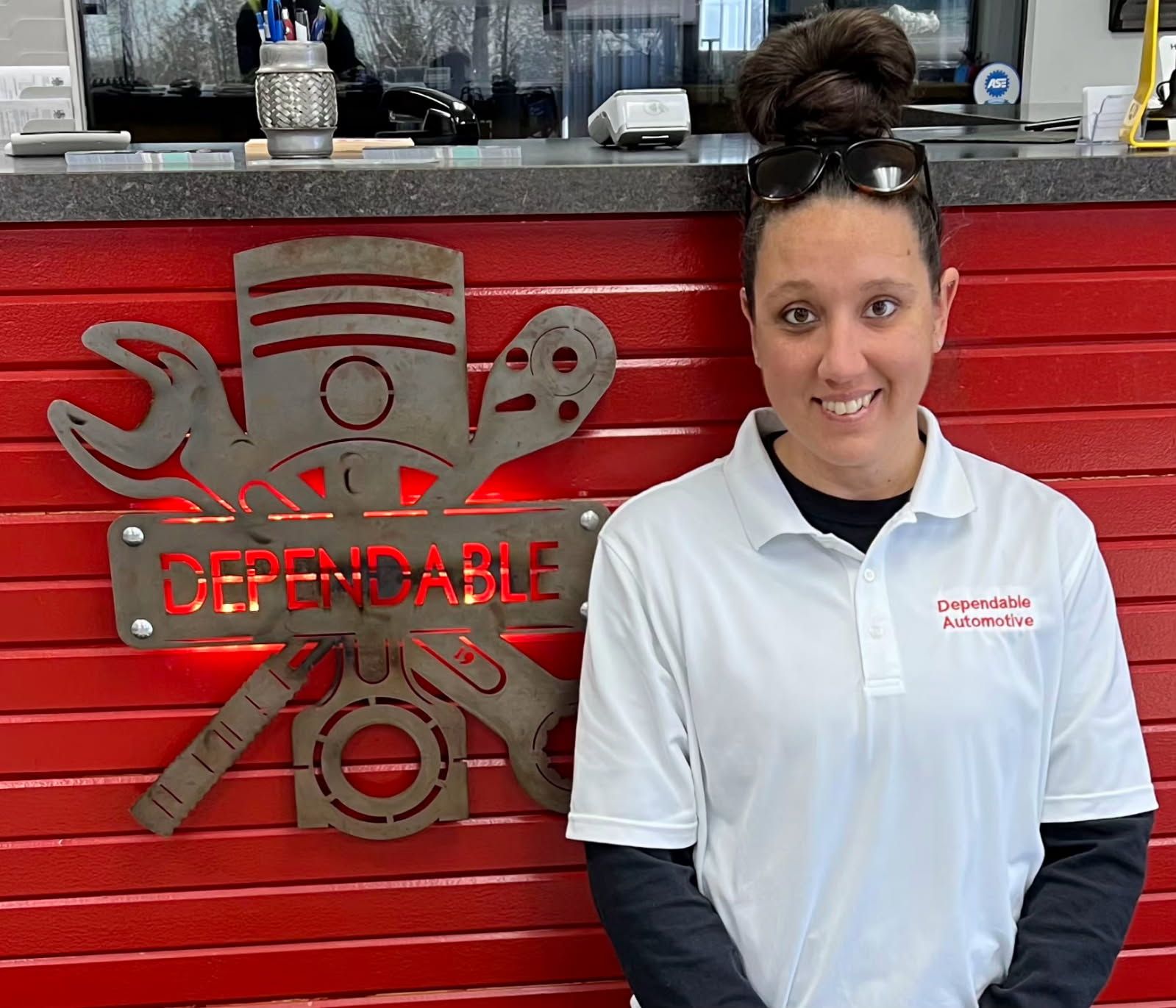Woman in white polo standing beside red “Dependable” tool-themed wall display. | Dependable Automotive
