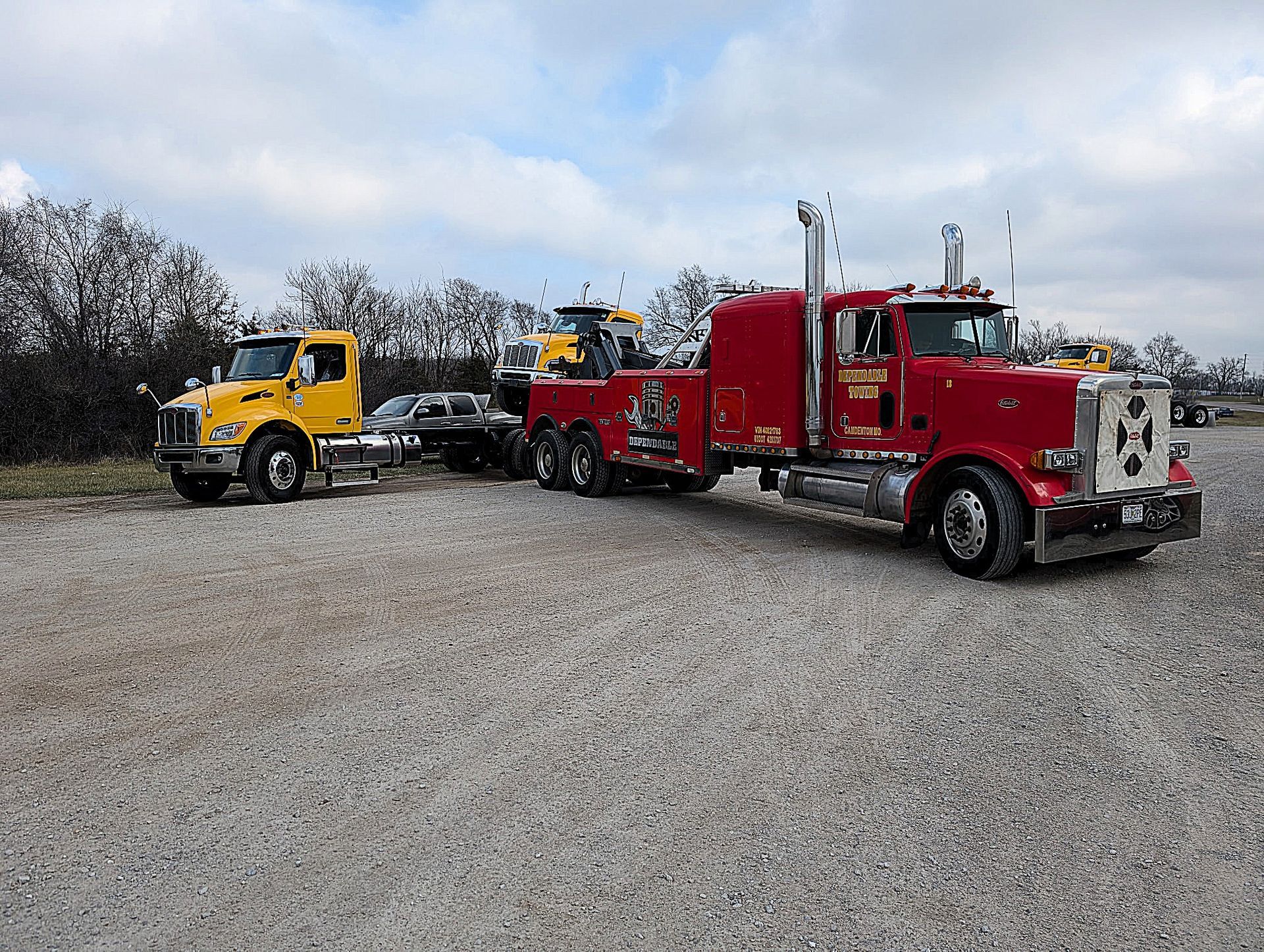 Red and yellow semi trucks parked on a gravel lot under a cloudy sky | Dependable Automotive