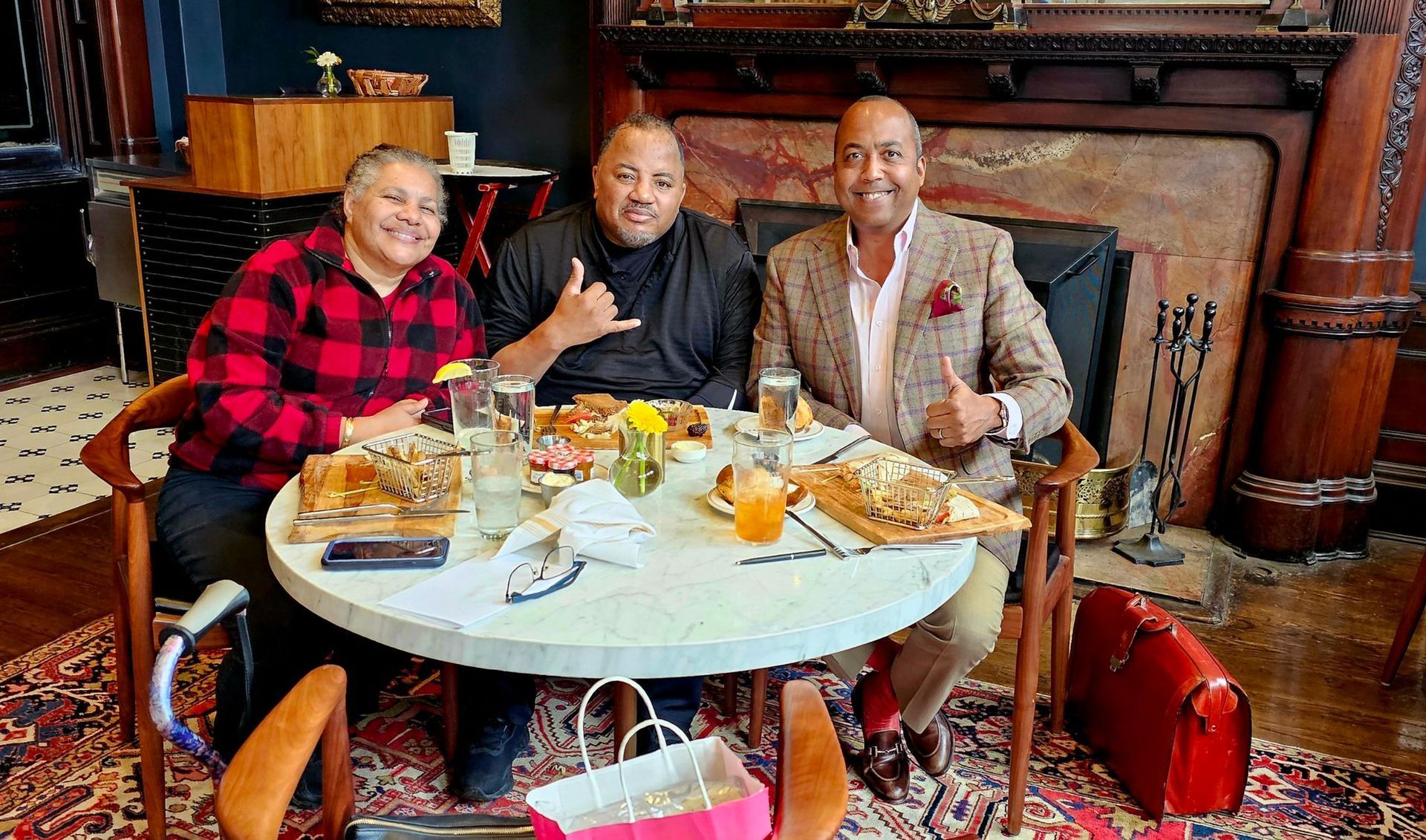 Three men are sitting at a table with food and giving a thumbs up.