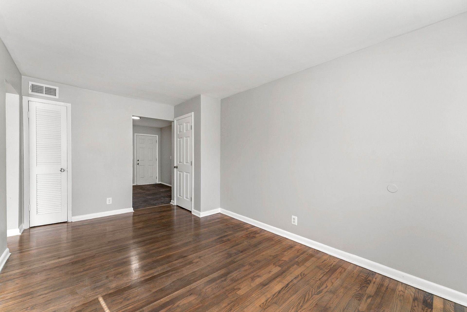 Empty room with hardwood floors, white walls, and a doorway leading to a hallway