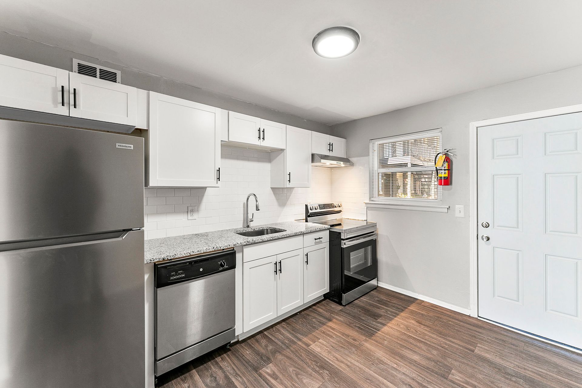 Bright modern kitchen with stainless steel appliances, white cabinets, and dark wood flooring