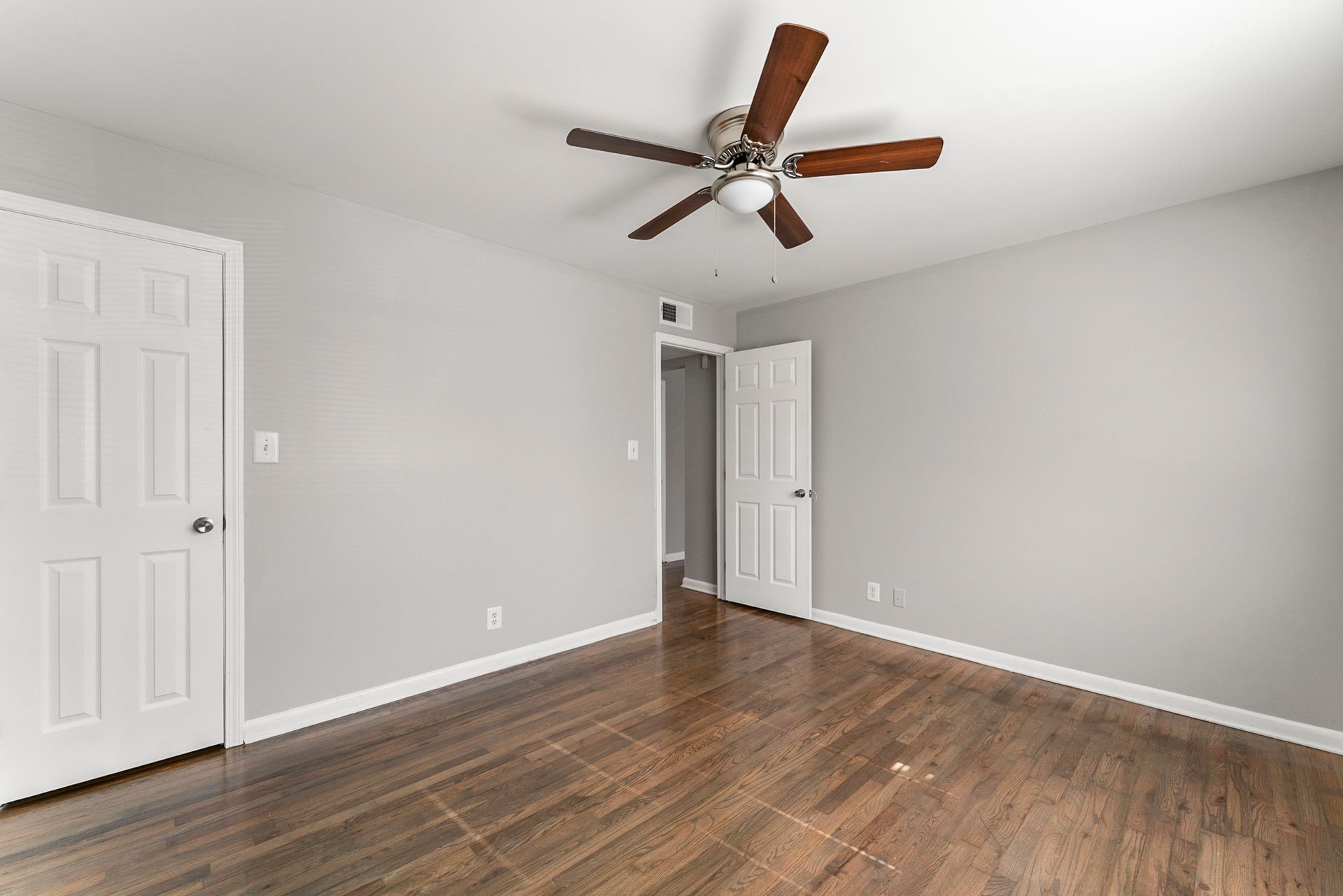 Empty gray bedroom with wood floor, white doors, and a ceiling fan.