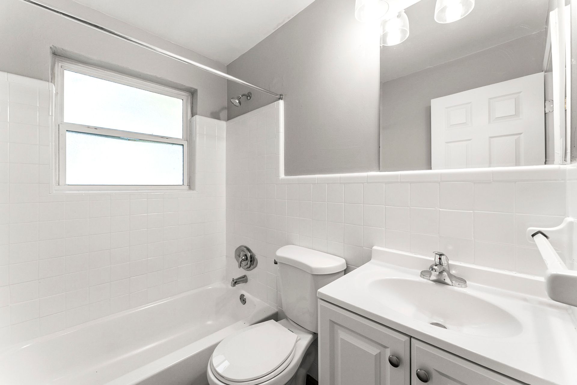 Small white bathroom with a tub, toilet, sink vanity, window, and large mirror