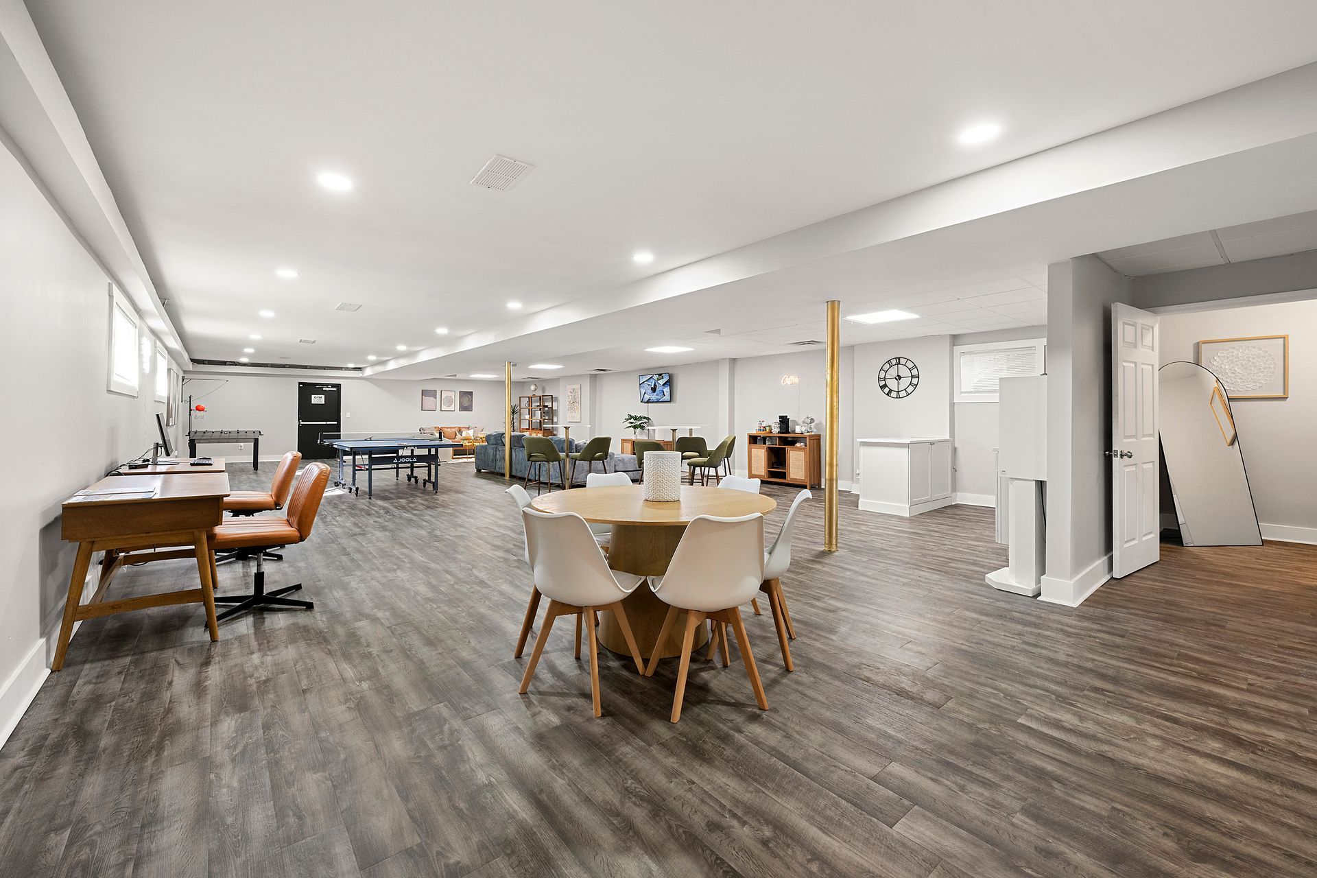 Bright open office lounge with tables, chairs, sofas, and wood flooring under recessed ceiling lights.