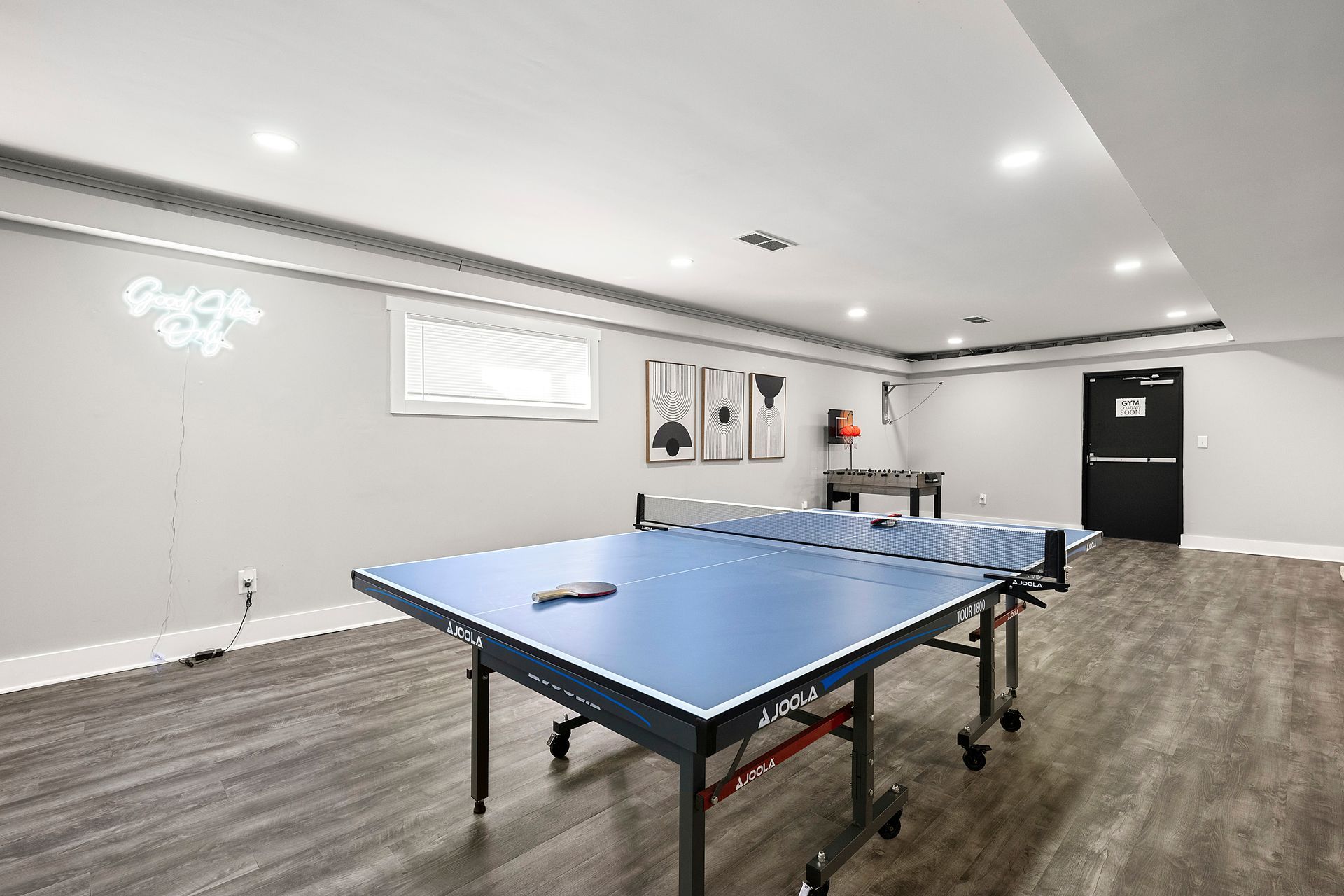 Empty basement rec room with a blue ping-pong table and gray wood flooring