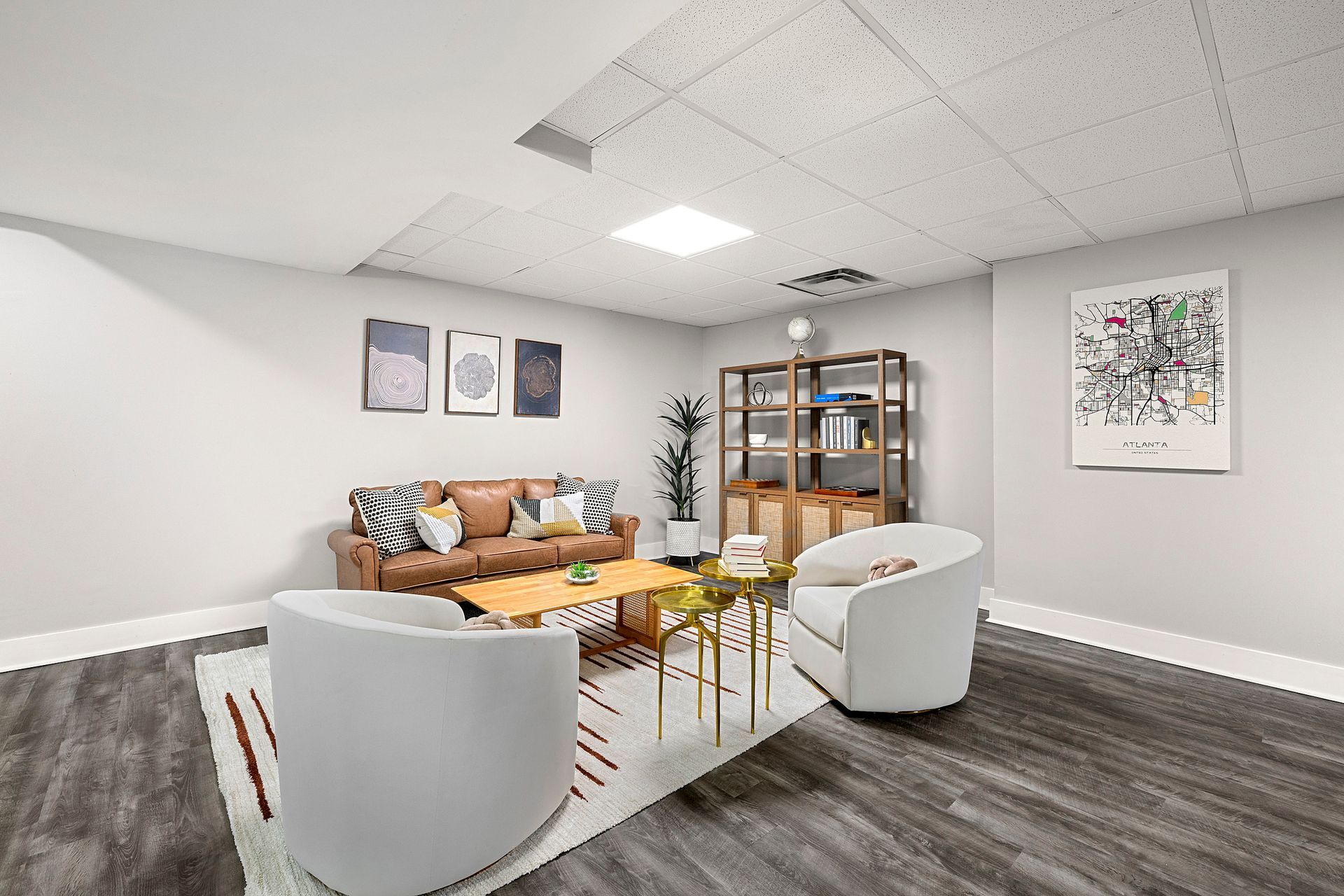 Modern lounge with white chairs, tan sofa, gold table, and shelving against gray walls and wood floor