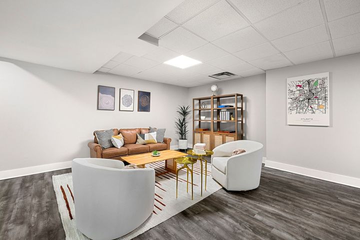 Modern lounge with white chairs, tan sofa, gold table, and shelving against gray walls and wood floor