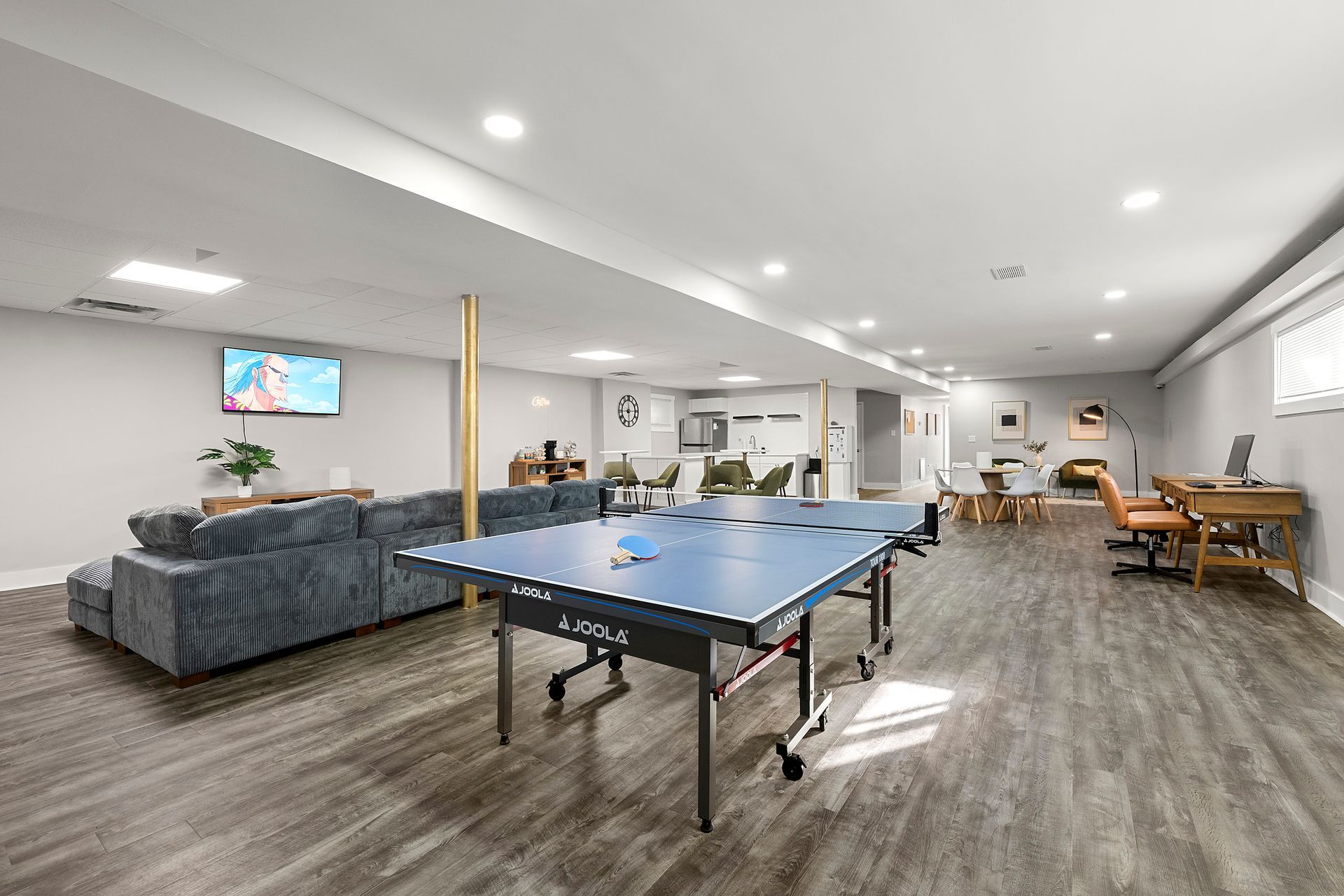 Spacious game room with ping-pong table, gray sectional sofa, wall TV, and dining area