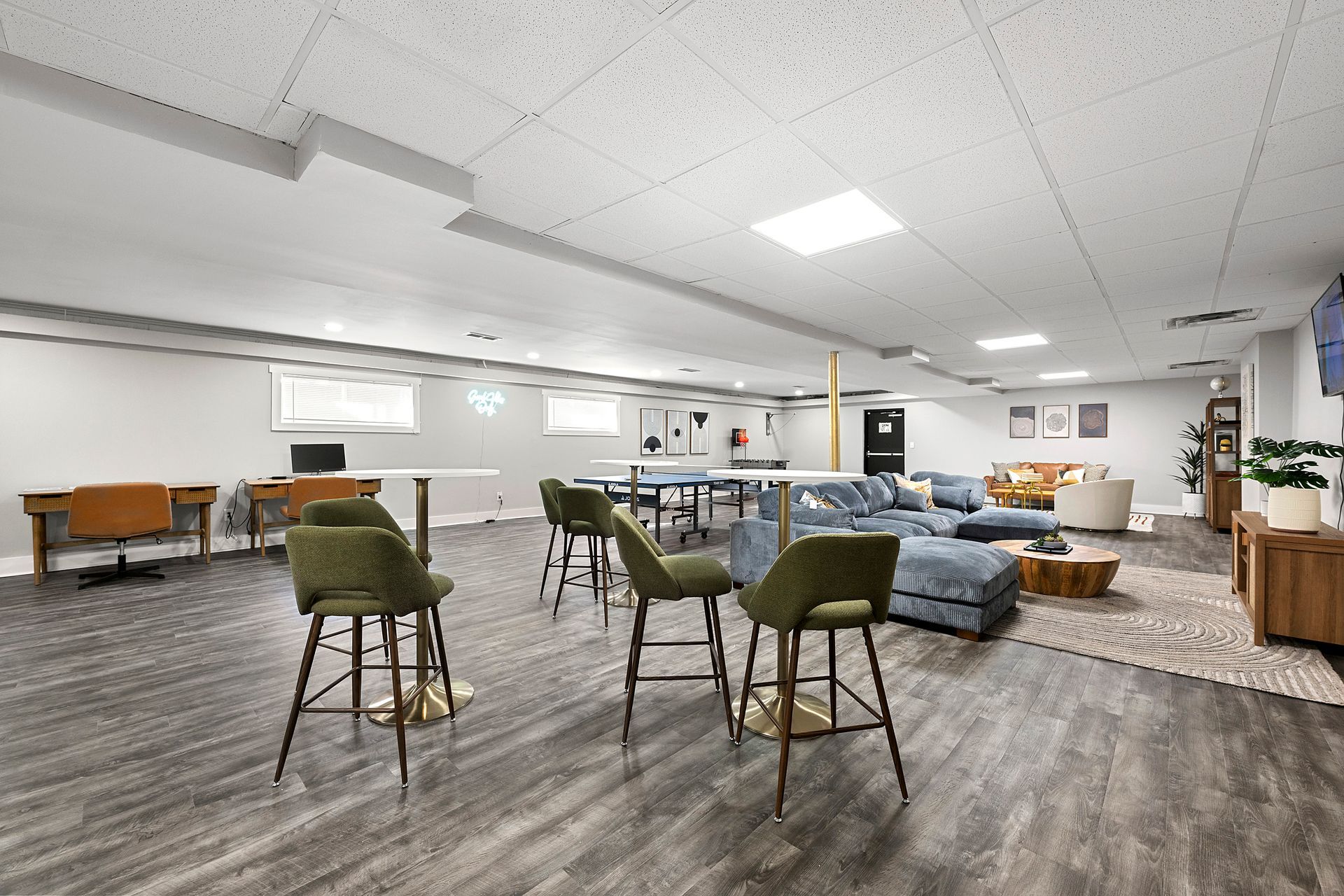 Spacious modern lounge with bar stools, tables, couches, and wood flooring under bright ceiling lights