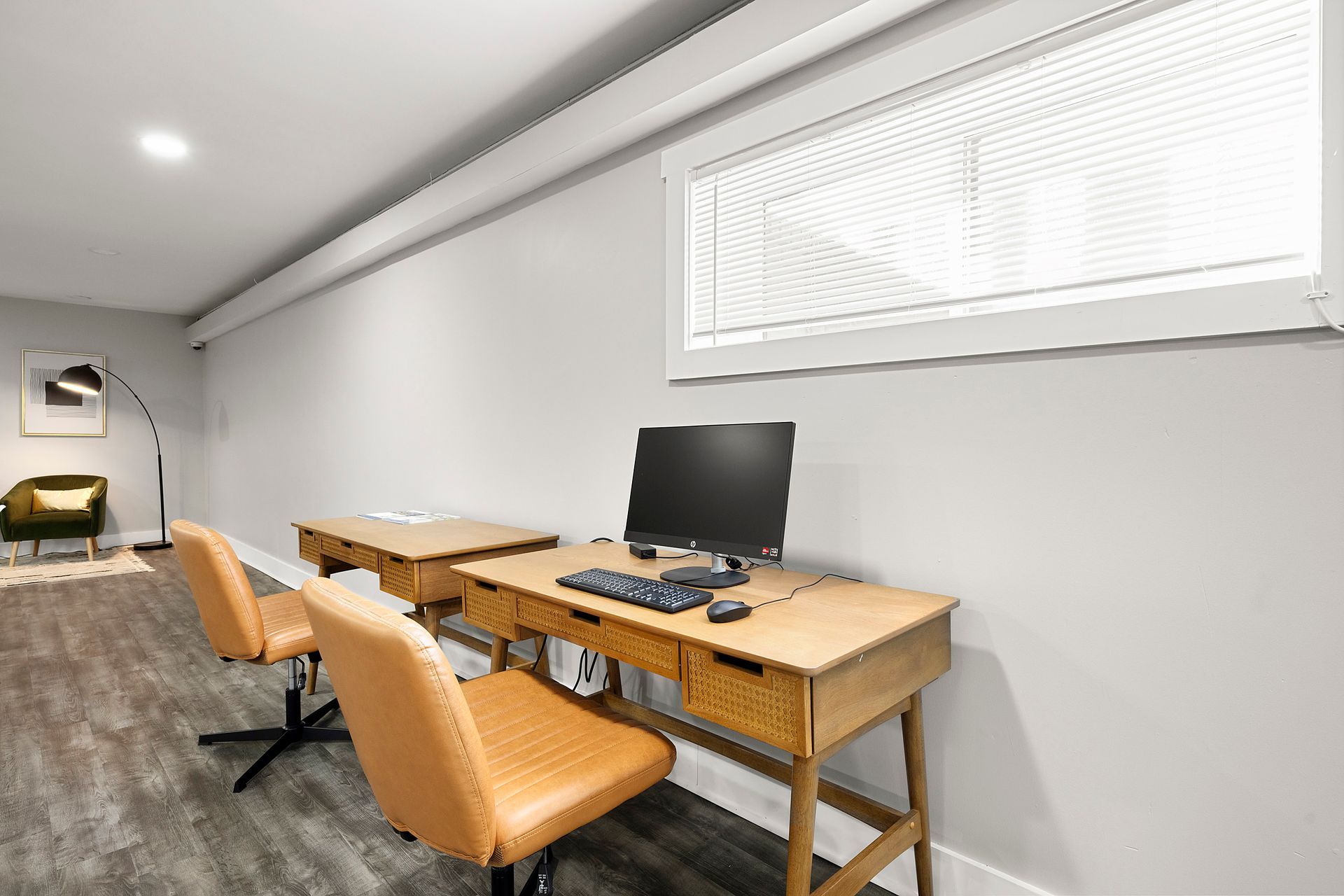 Quiet office with two wooden desks, orange chairs, a computer, and a large window blind.