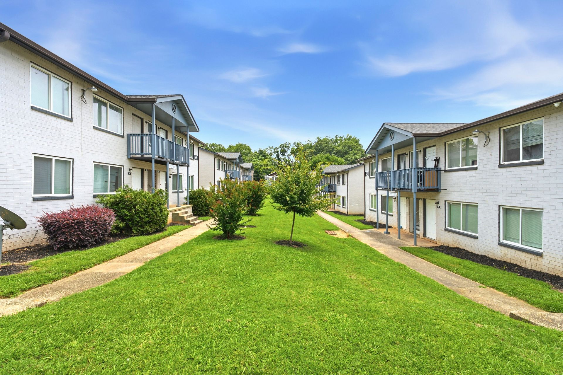 Apartment complex courtyard with green lawn, walkways, and white buildings on both sides