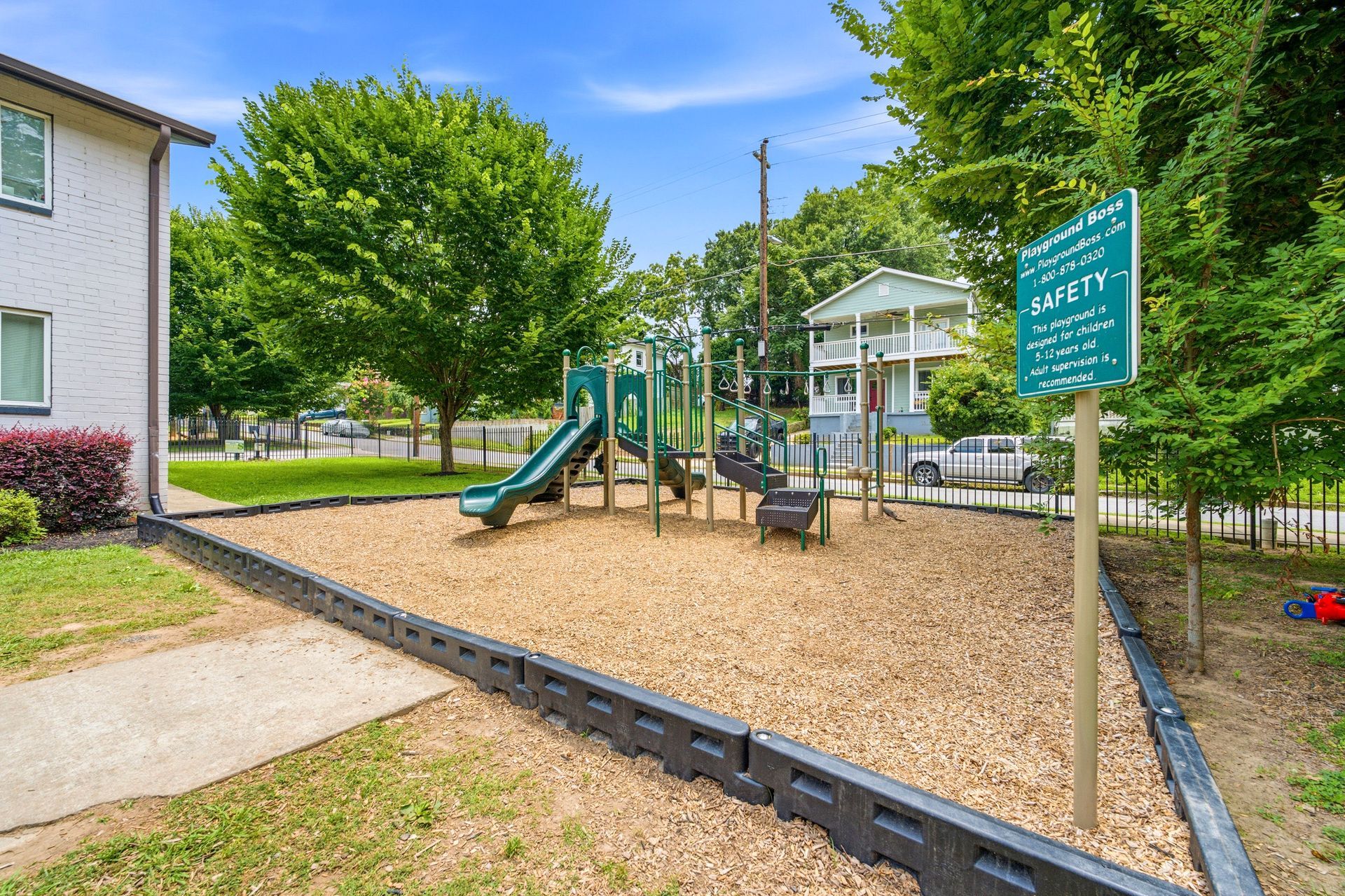 Apartment playground with slide, climbing structure, and green sign beside a building