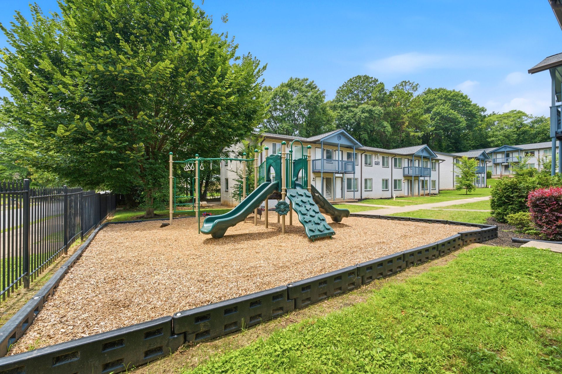 Playground with green slides and wood chips beside apartment buildings and trees