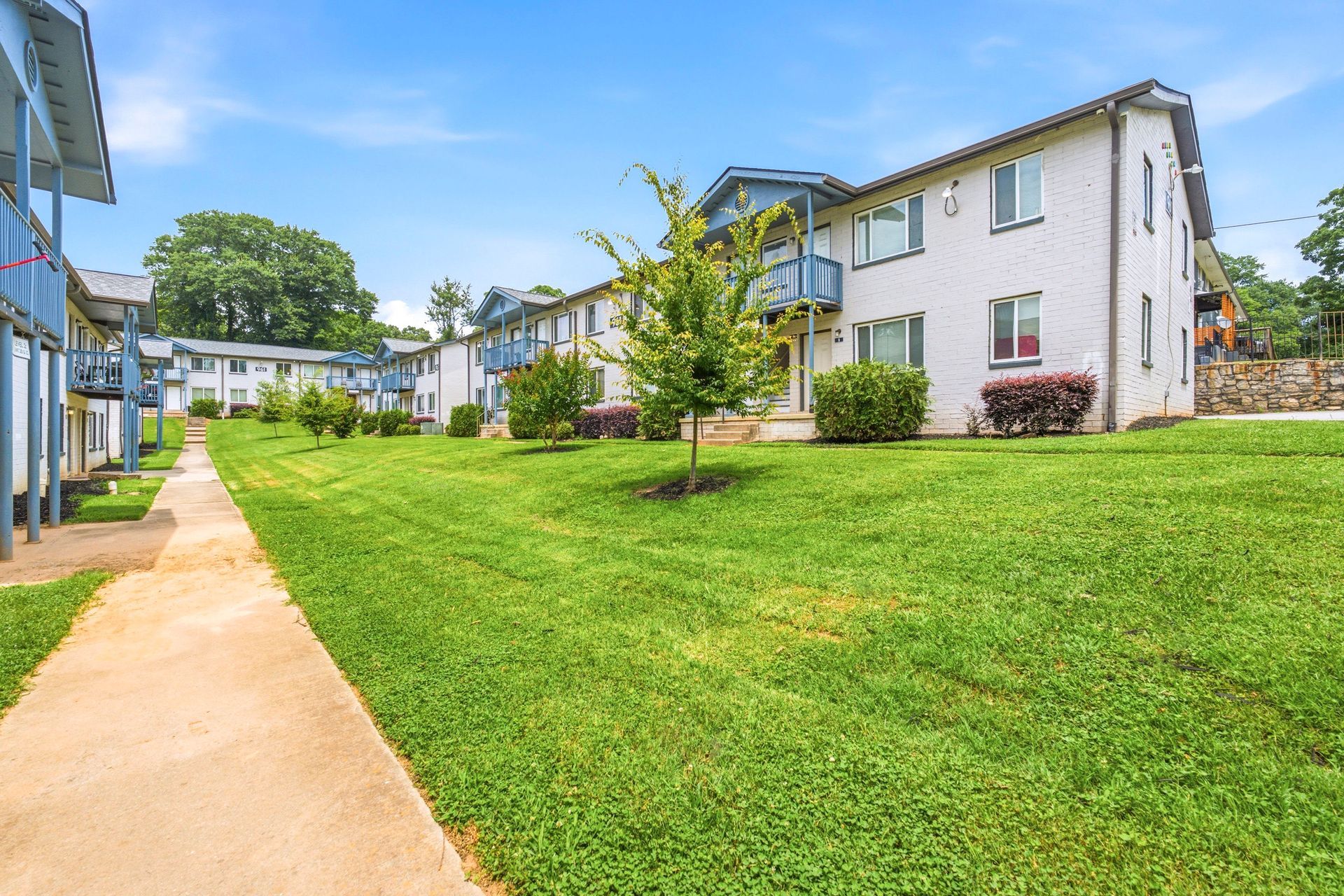 Apartment complex with white buildings, green lawn, and sidewalk under a blue sky
