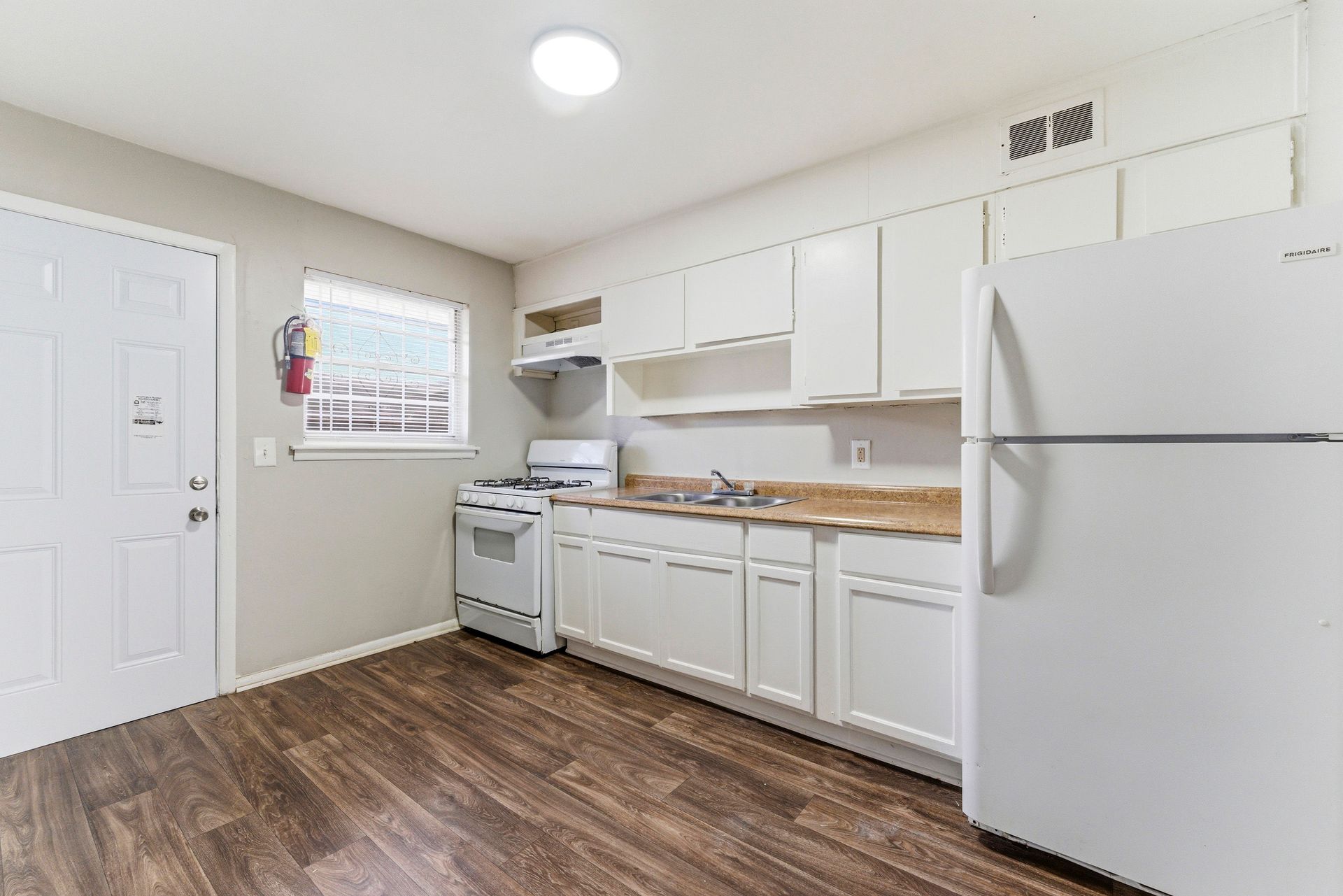 Bright kitchen with white cabinets, wood flooring, stove, refrigerator, and a small window.