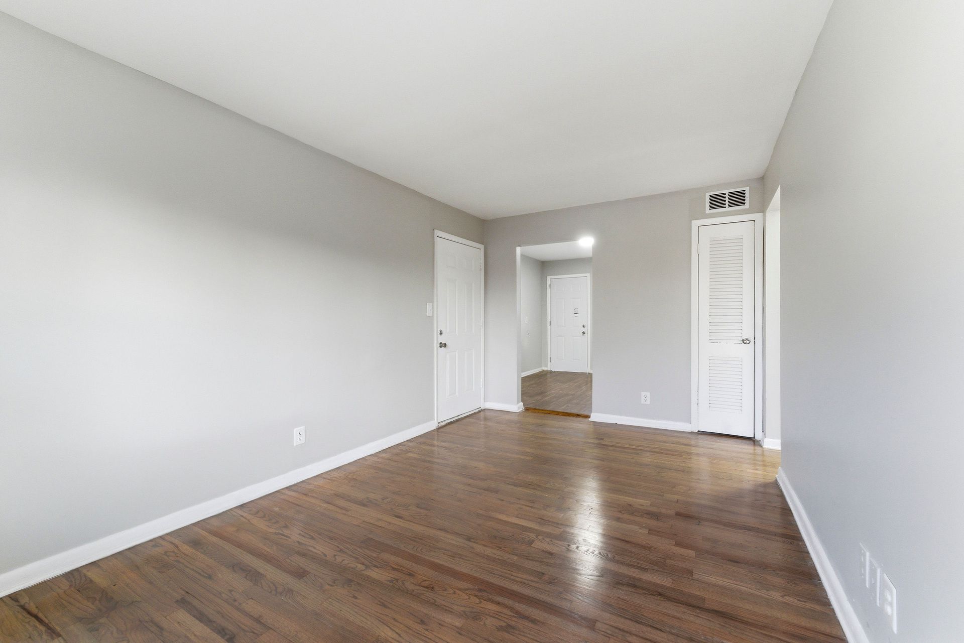 Empty room with gray walls, hardwood floor, white closet doors, and a doorway to a hall.