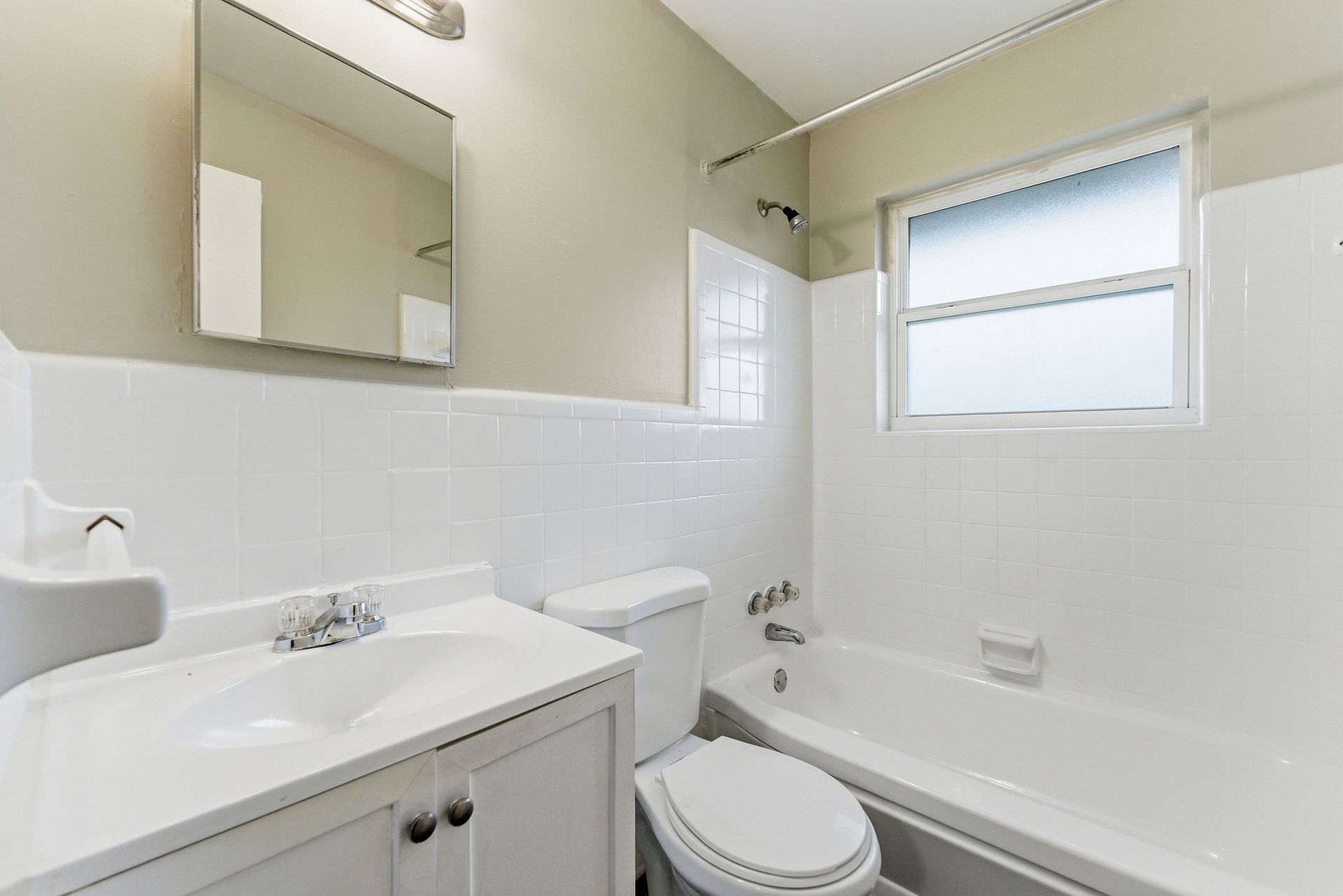 Bright white bathroom with vanity, toilet, mirror, and frosted window