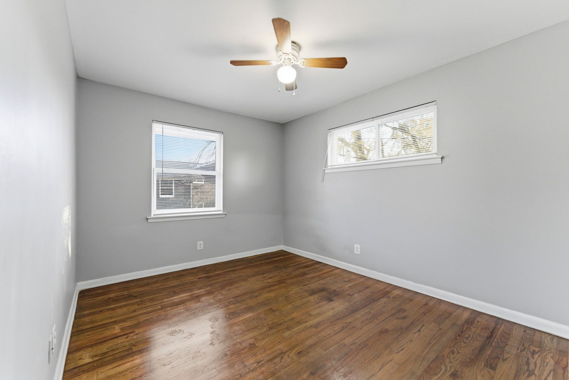 Empty gray bedroom with hardwood floors, white trim, and a ceiling fan