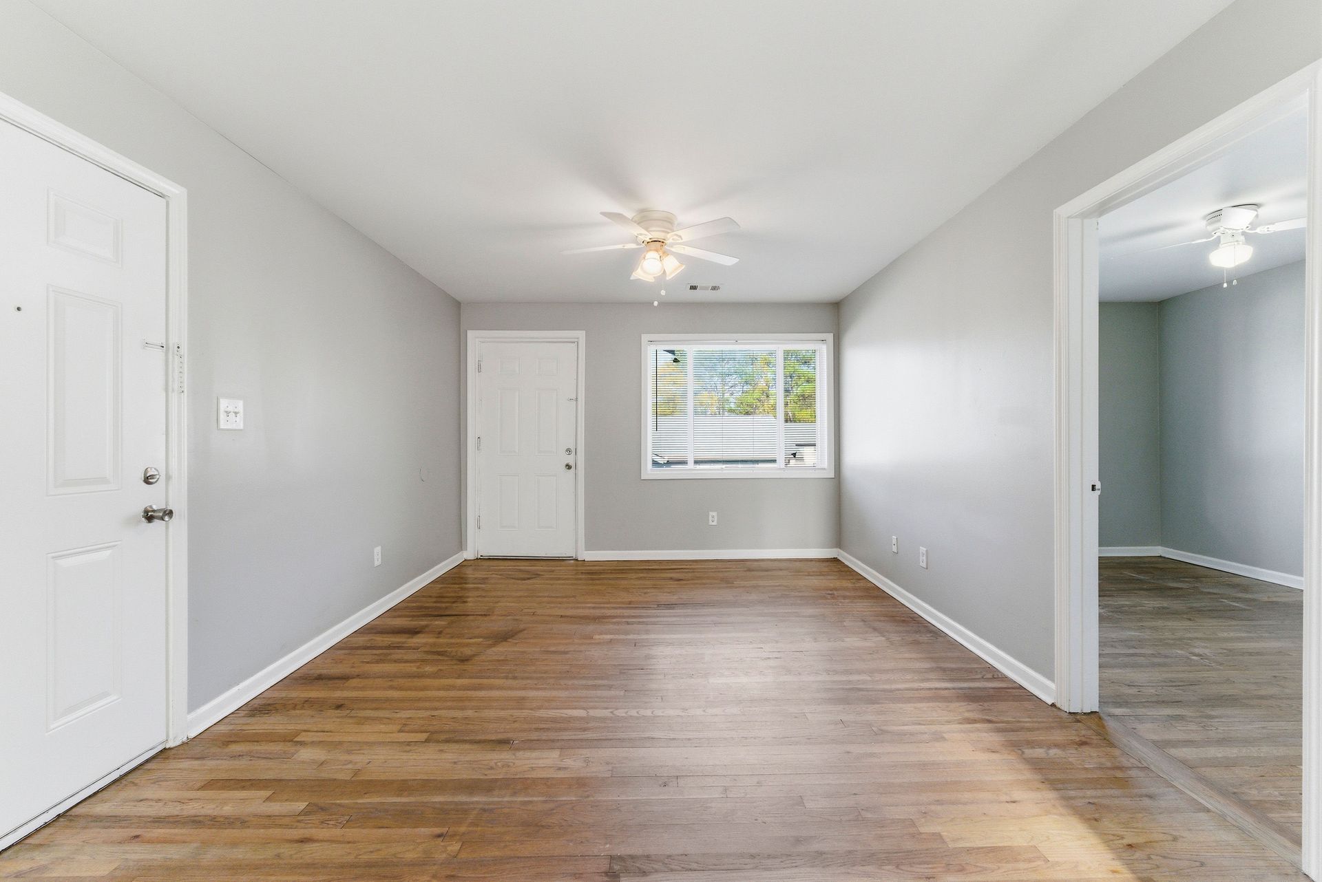 Empty white room with hardwood floors, a ceiling fan, and a window