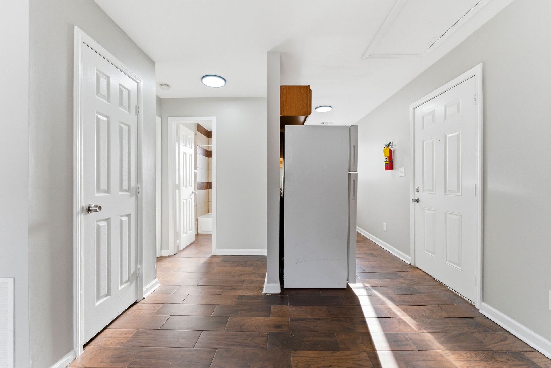 Bright hallway with white doors, gray walls, dark wood floors, and a central column under ceiling lights