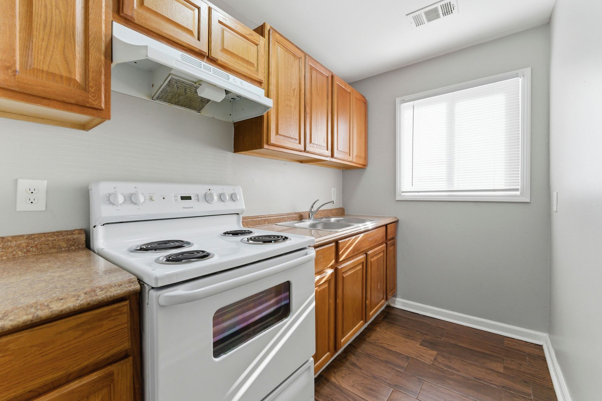 Bright kitchen with white stove, wood cabinets, beige counters, and a window.
