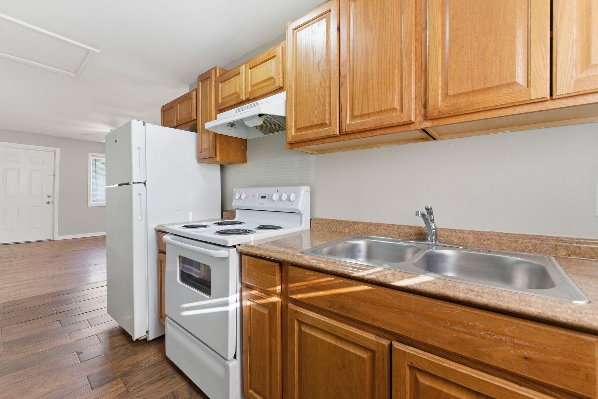 Bright kitchen with white appliances, wooden cabinets, and double sink along a narrow wall