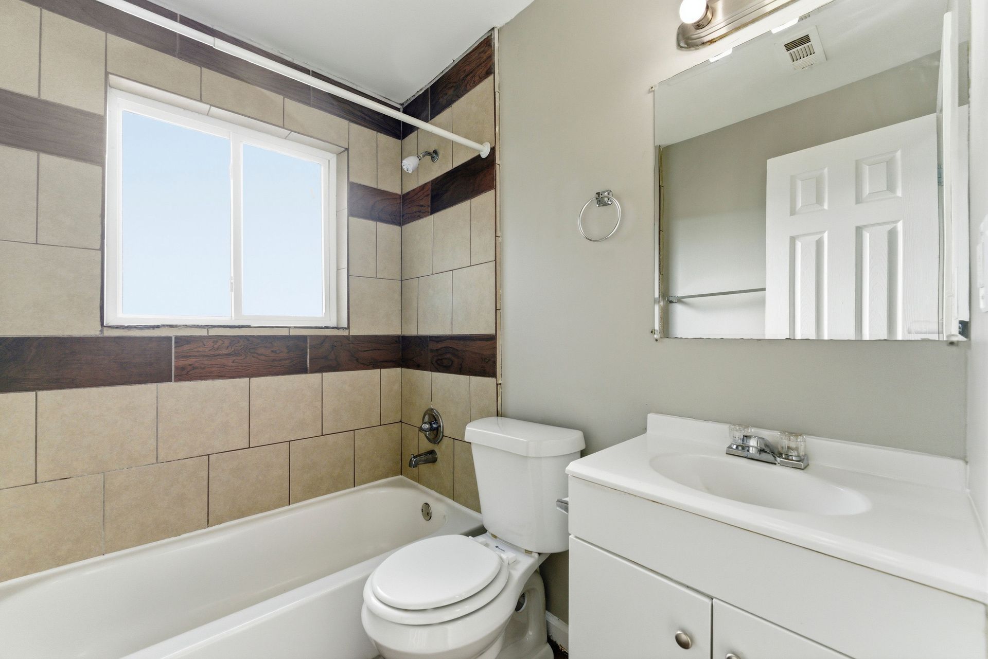 Bright bathroom with bathtub, toilet, sink vanity, and large mirror by a window.