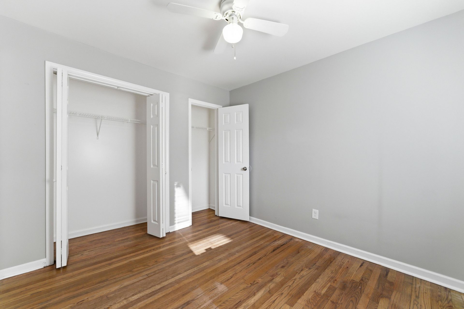 Empty bedroom with gray walls, hardwood floors, open closet, and a ceiling fan.