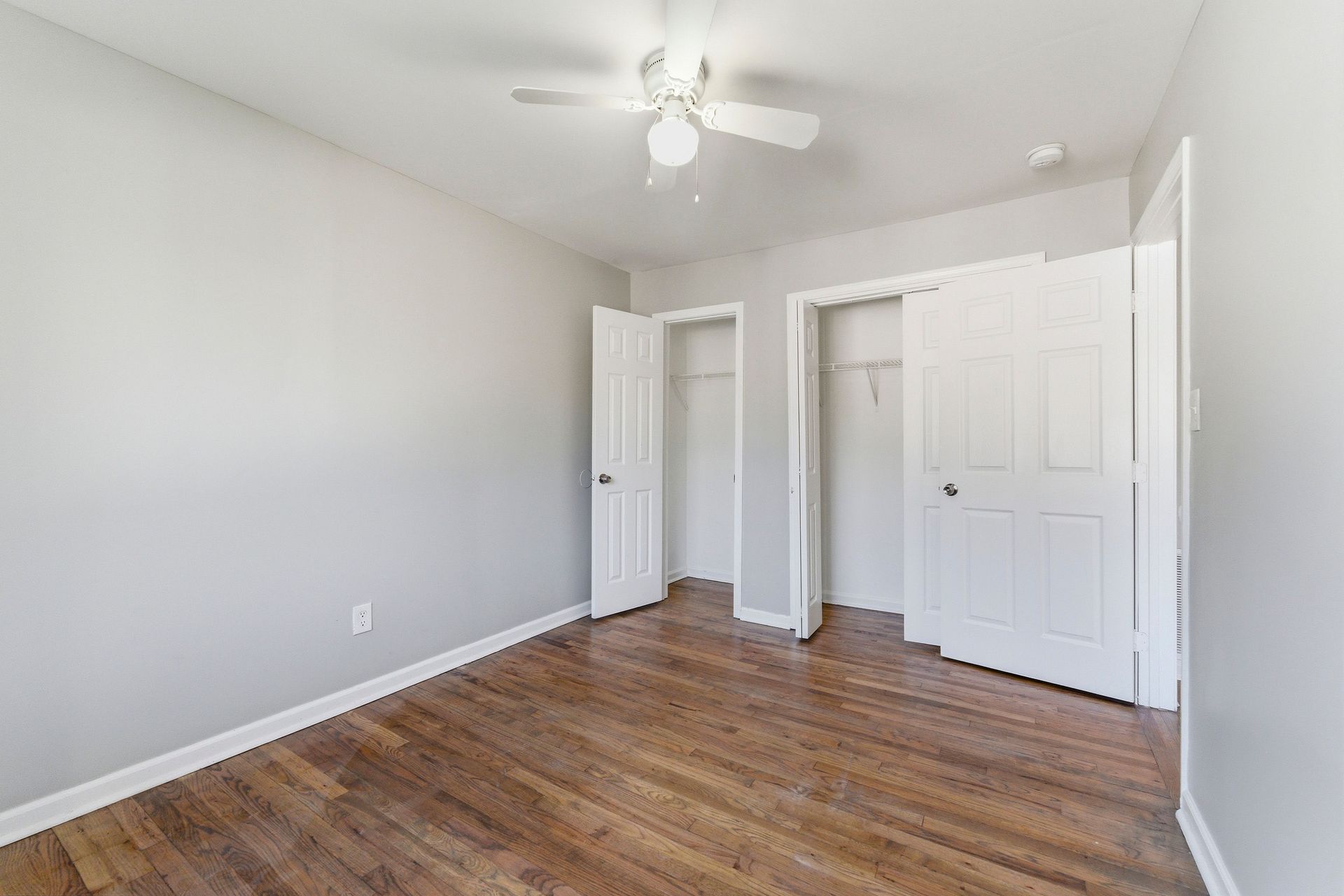 Empty white bedroom with wood floor, ceiling fan, and open closet doors