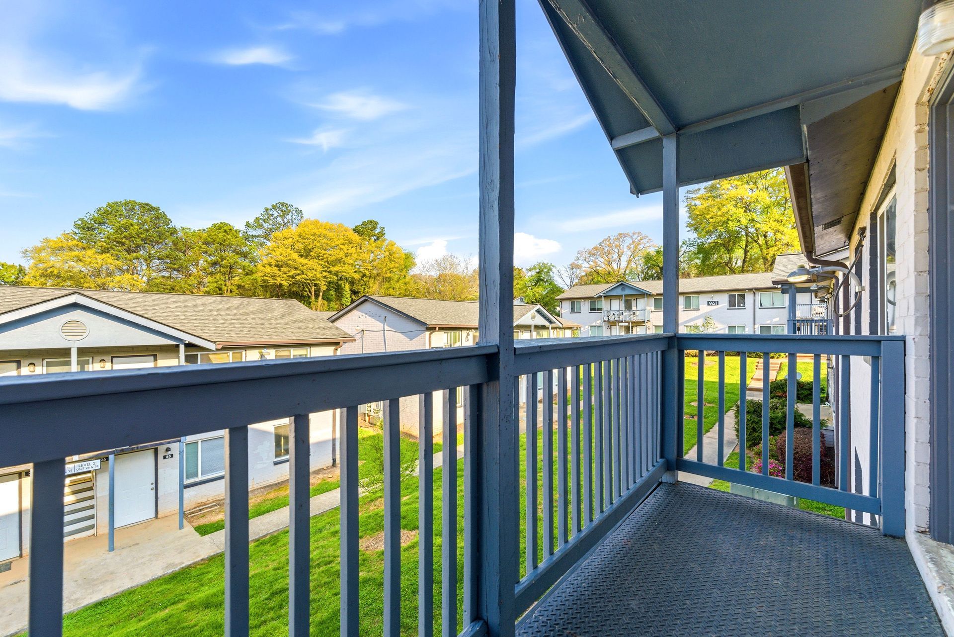 Apartment balcony overlooking a grassy courtyard and neighboring buildings on a sunny day