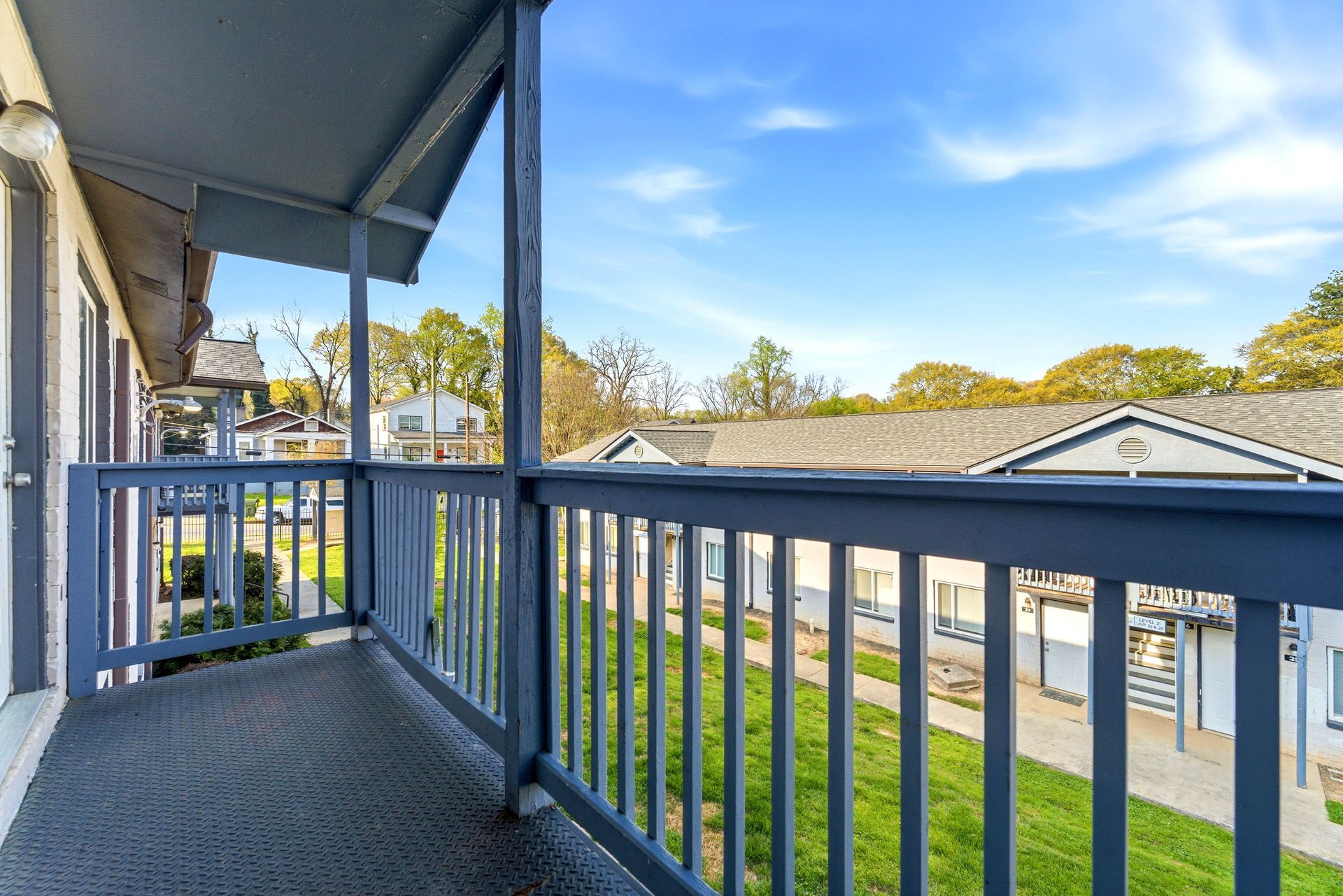 Apartment balcony with blue railing overlooking a courtyard and low buildings under a bright sky