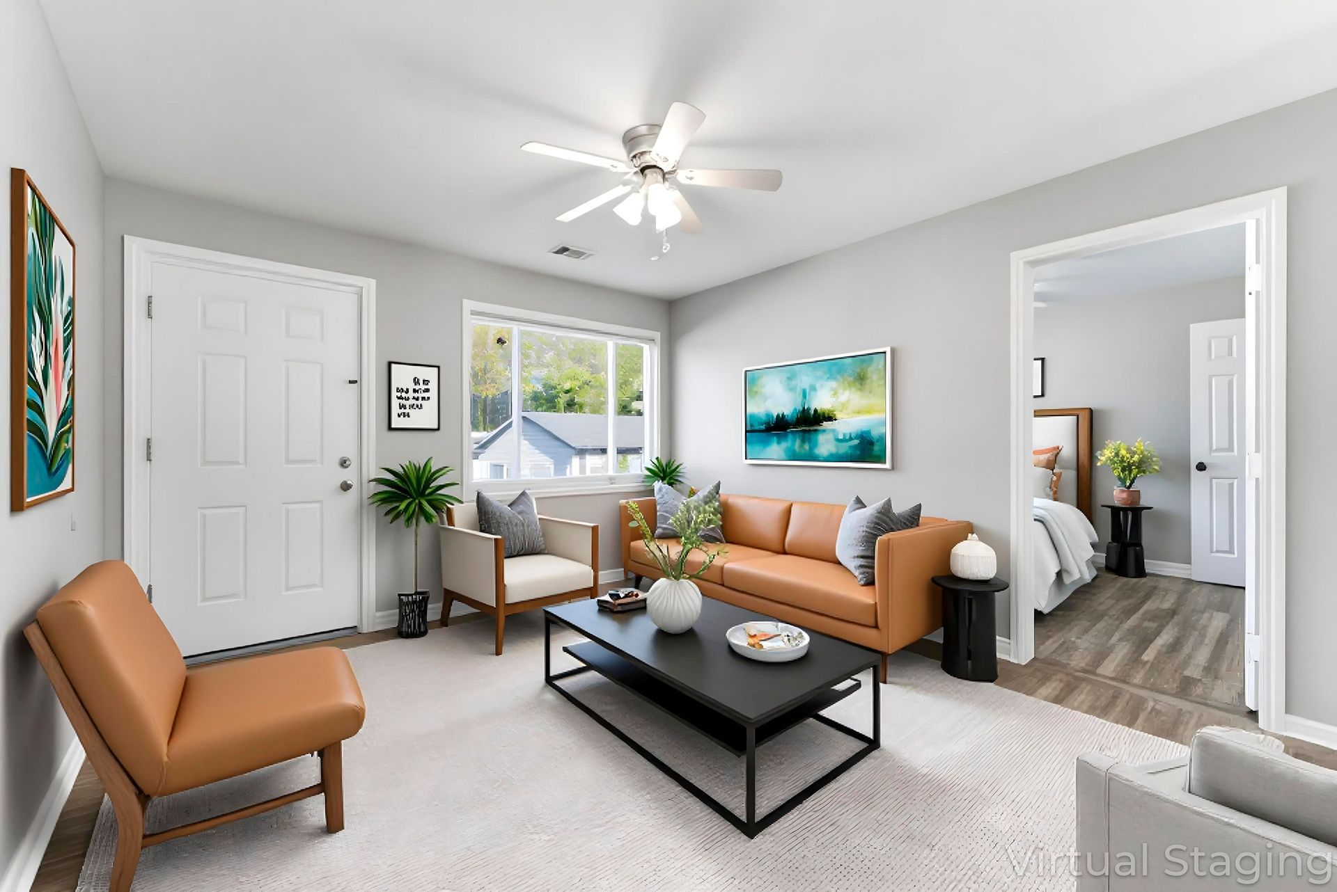 Bright living room with tan sofa, black coffee table, chair, wall art, and adjoining bedroom visible through doorway