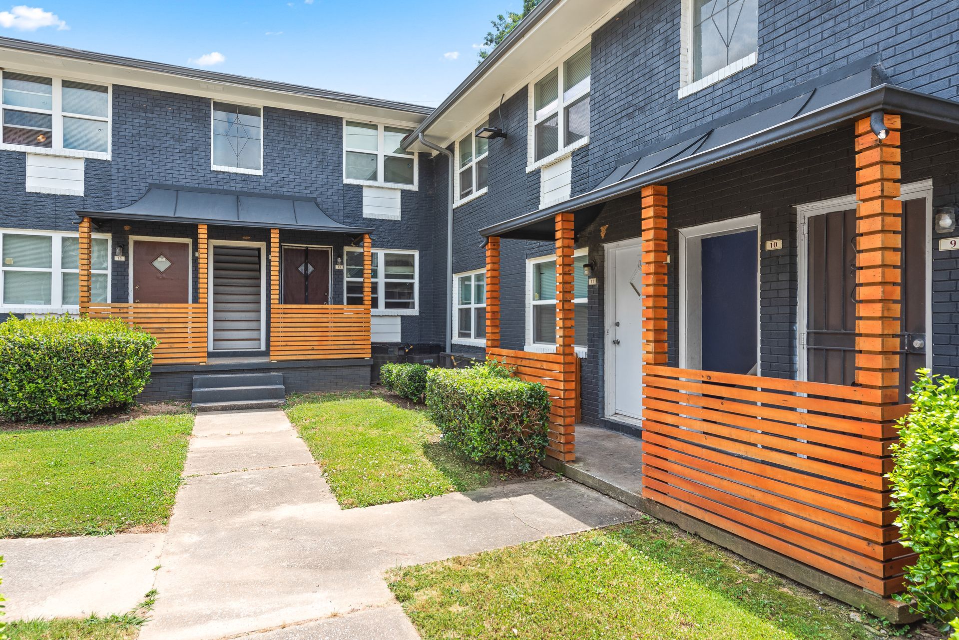 Courtyard of modern apartment buildings with brick columns, wood railings, and a central walkway