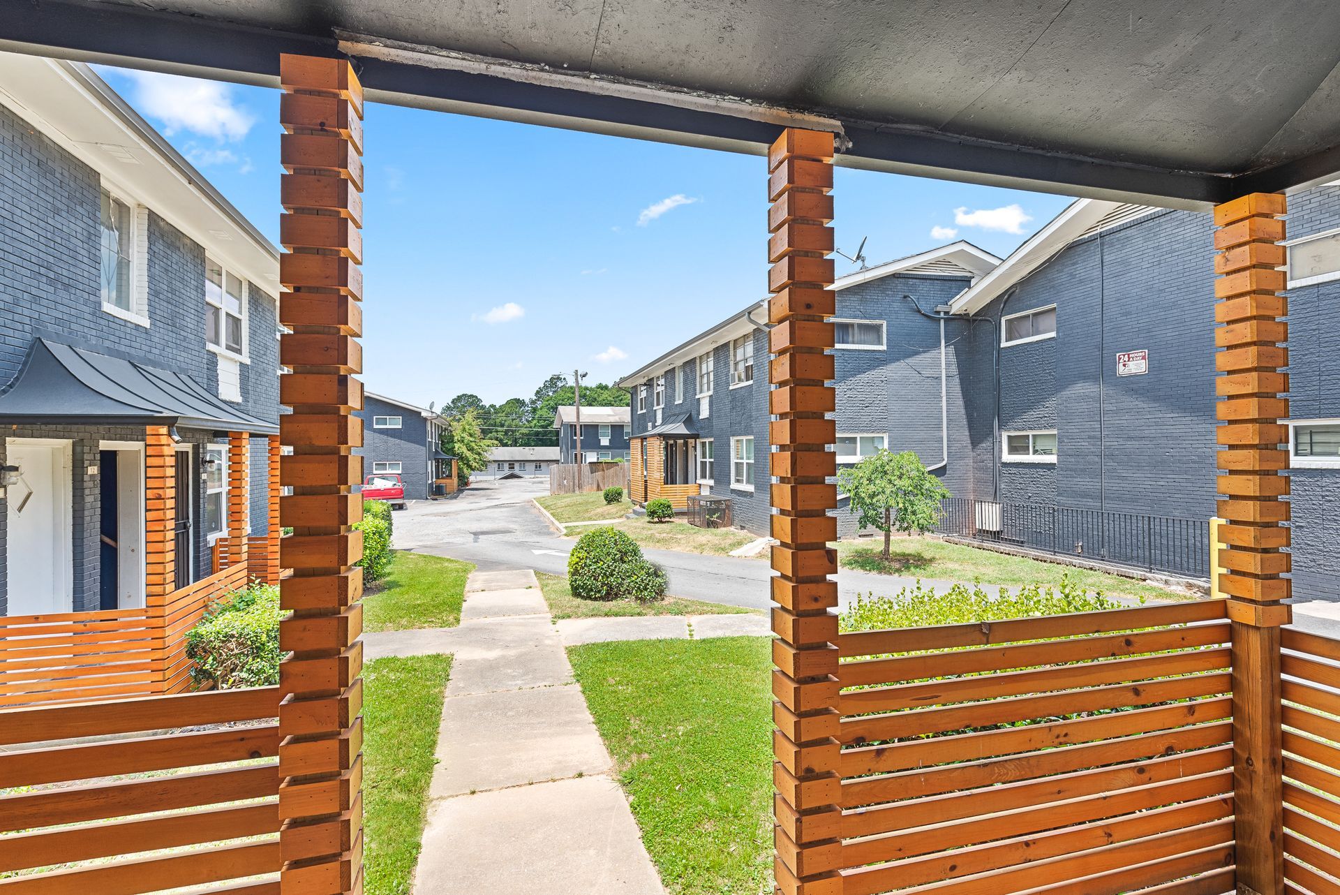Covered porch view of apartment buildings, a walkway, grass, and a sunny courtyard