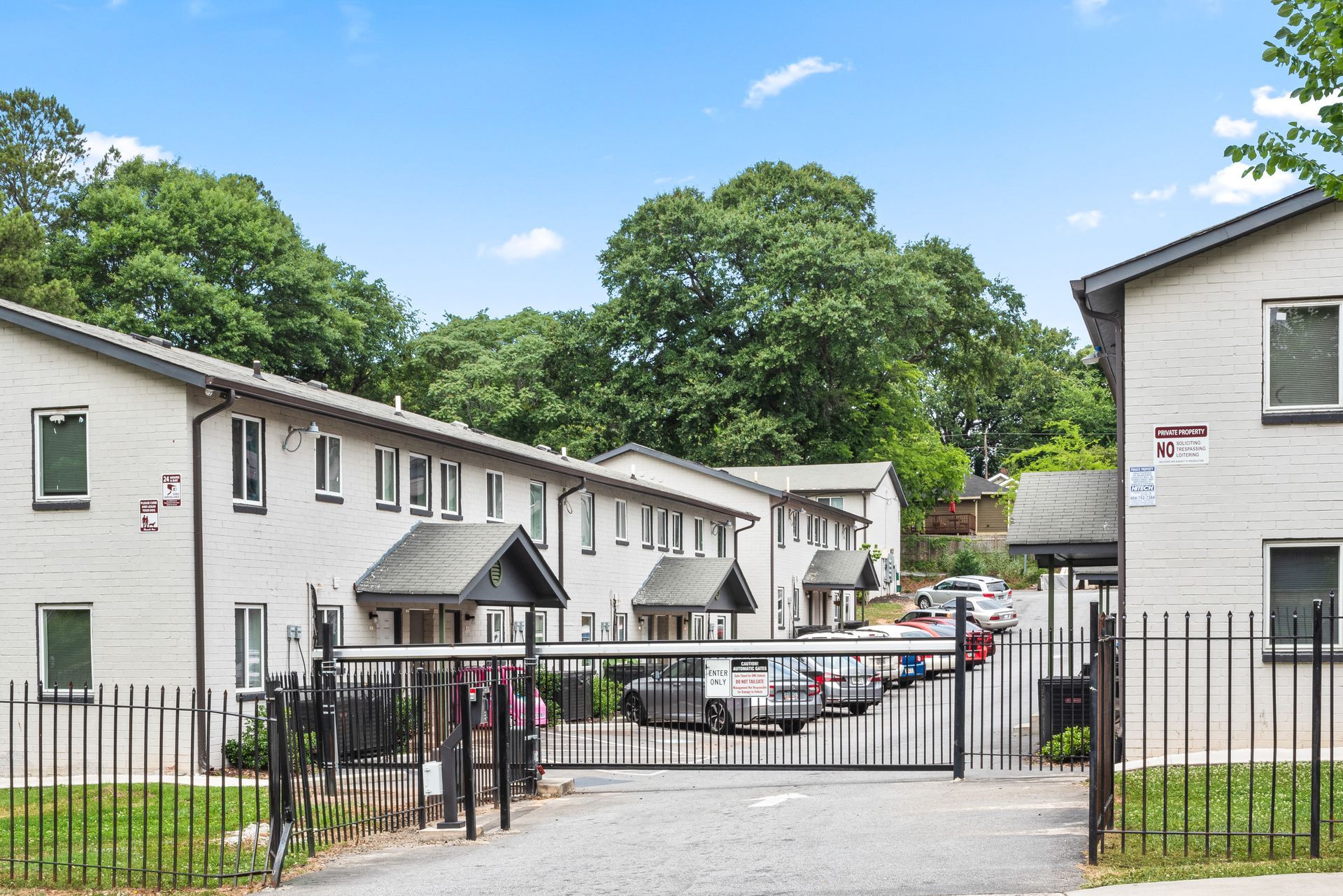 Gated apartment courtyard with parked cars and white buildings under a blue sky