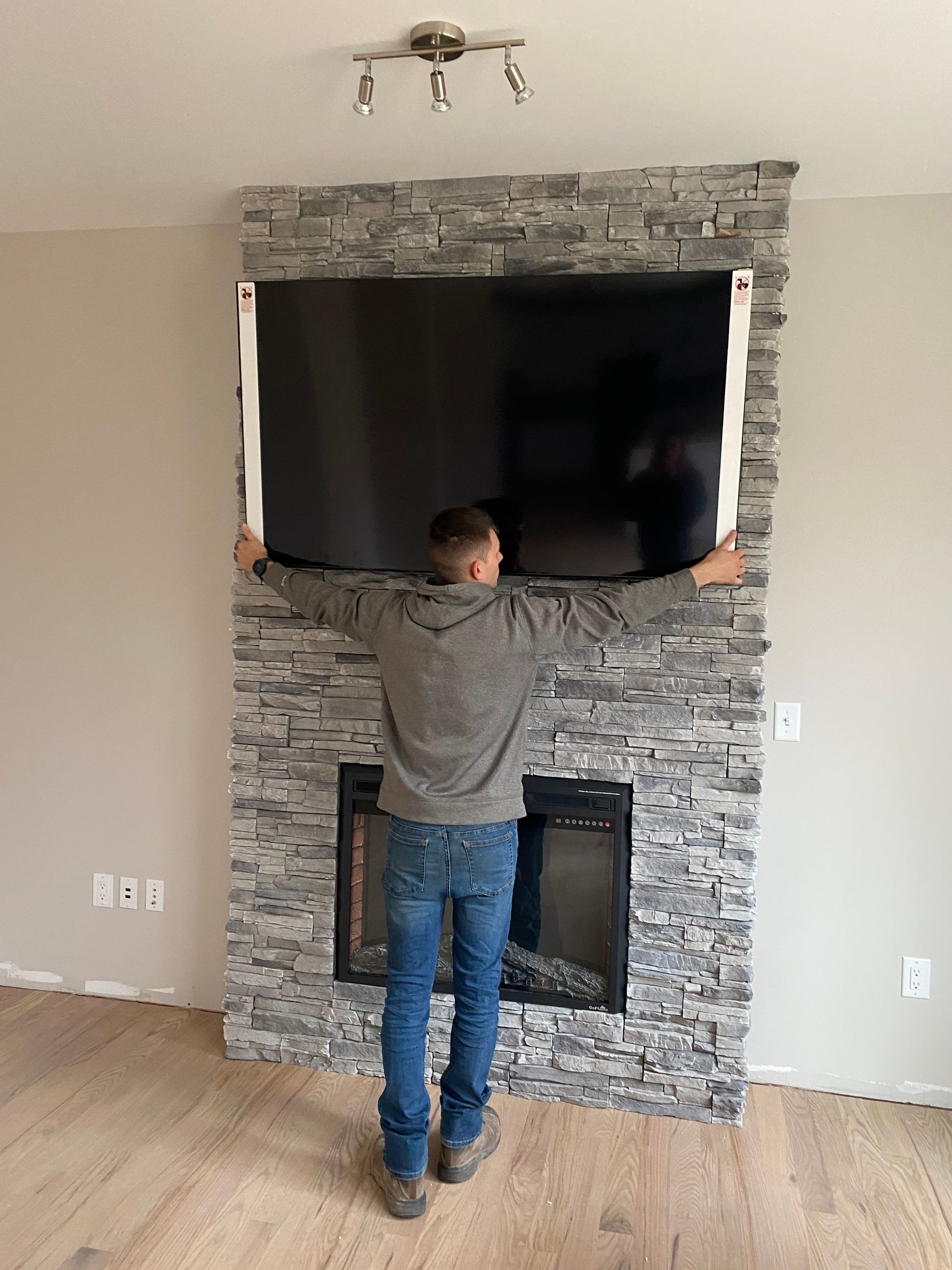 A man is holding a flat screen tv over a fireplace.