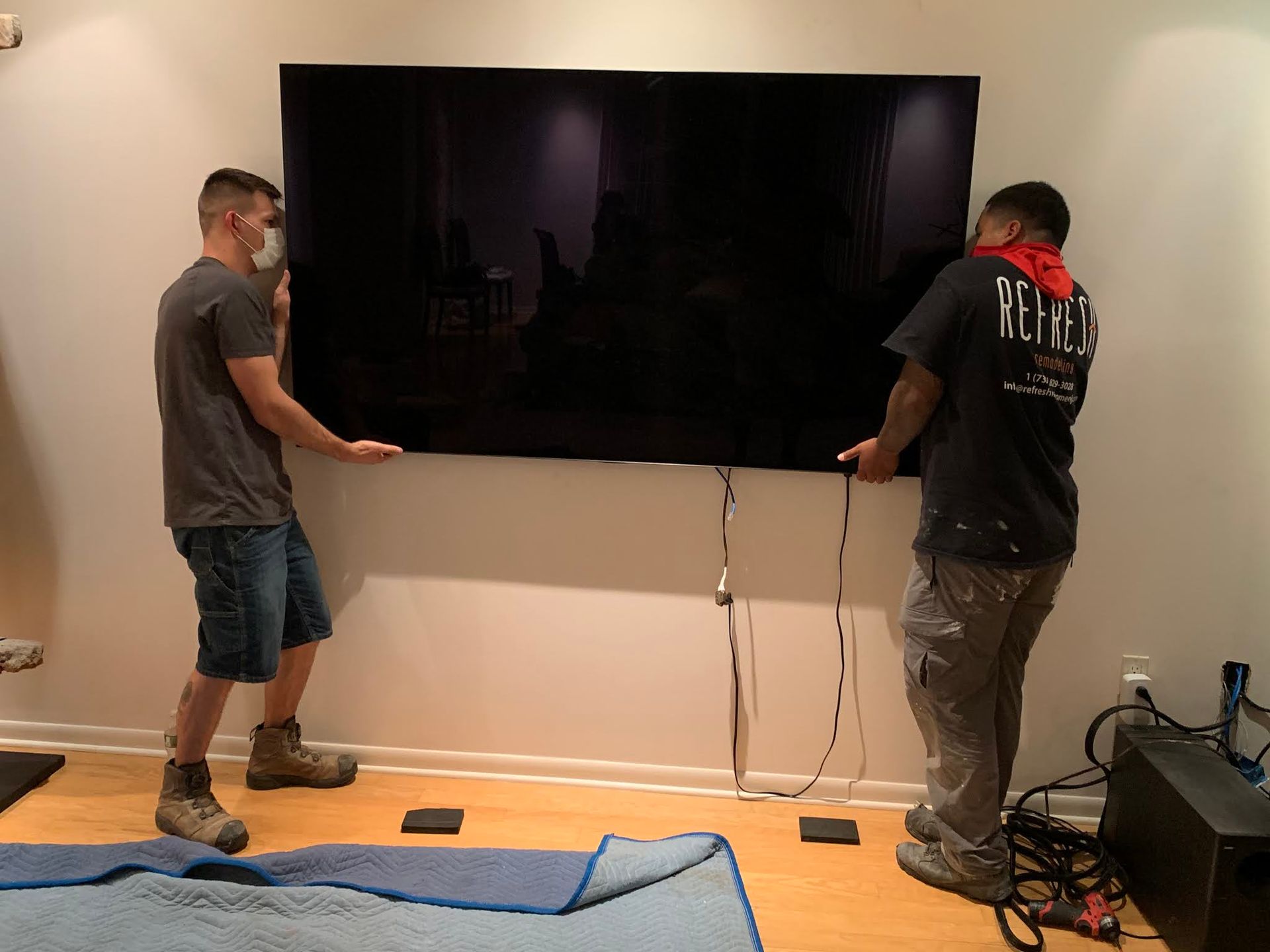 Two men are installing a flat screen tv in a living room