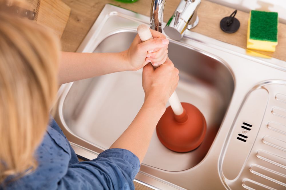 A Woman is Using a Plunger to Unblock a Sink — Nightcliff Plumbing & Gas In Coconut Grove, NT