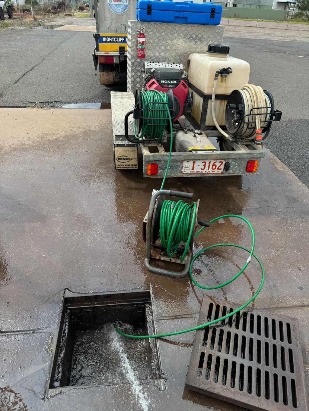 Utility truck with hose reels pumping water into an open drain beside a wet street — Nightcliff Plumbing & Gas In Coconut Grove, NT