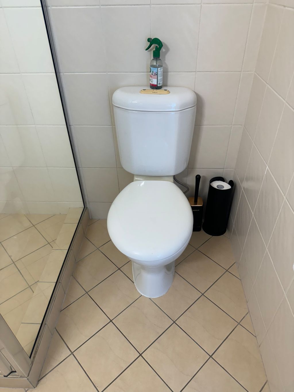 Small bathroom with a white toilet and beige tiled floor, viewed through a partially open shower door — Nightcliff Plumbing & Gas In Parap, NT