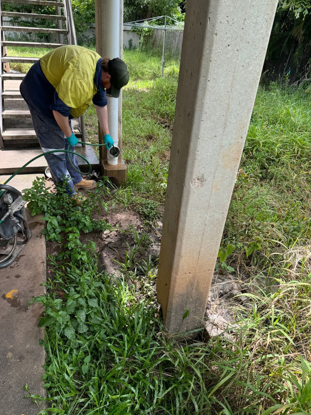 Person kneeling outdoors, digging soil beside a concrete pillar and stairs with a hand tool — Nightcliff Plumbing & Gas In Coconut Grove, NT