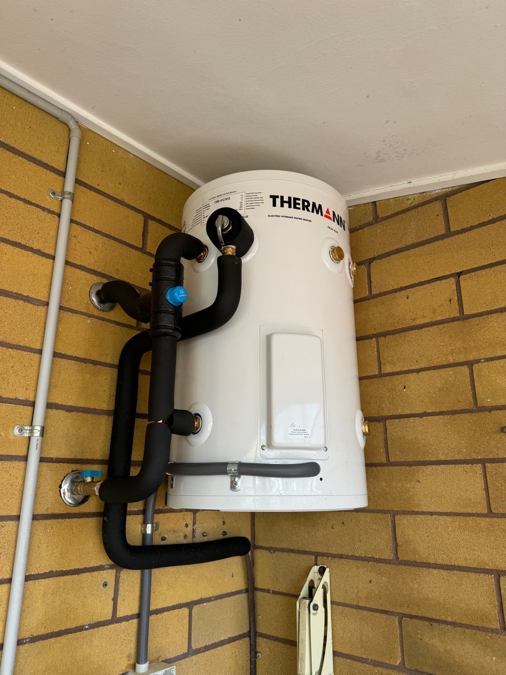White hot water heater with black pipes mounted in a brick-walled utility corner — Nightcliff Plumbing & Gas In Coconut Grove, NT