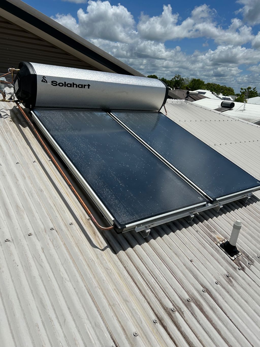 Solar water heater and rooftop solar panels on a corrugated metal roof under a cloudy sky — Nightcliff Plumbing & Gas In Coconut Grove, NT