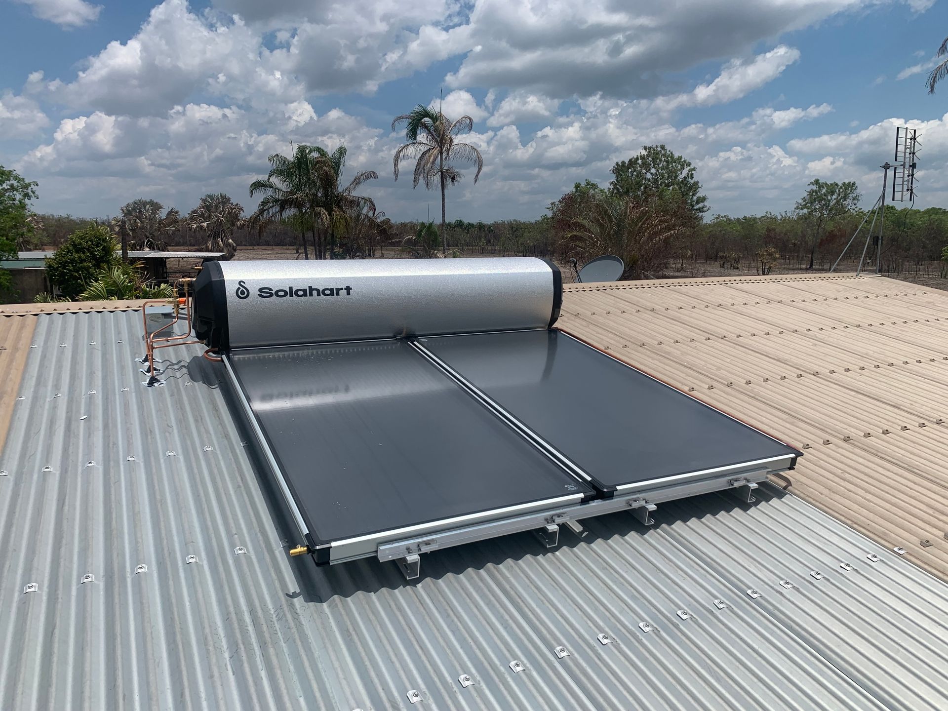 Solar water heater installed on a corrugated metal roof under a partly cloudy sky — Nightcliff Plumbing & Gas In Coconut Grove, NT